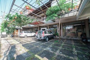 A covered outdoor area with two cars parked, a building entrance, and a glass ceiling structure. - Blok O International Guest House by MHM (Banguntapan)