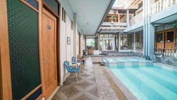 A hotel corridor with a pool, wooden doors, and a seating area.