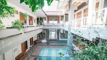 Un espacio interior de varios niveles con una piscina central, balcones y plantas de interior.