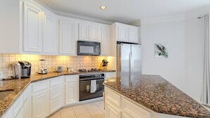 A modern kitchen with white cabinetry, a stainless steel refrigerator, a microwave, a toaster, and a blender. - Cozy Townhouse near Midtown (Houston)