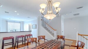 A dining area with a glass-top table, wooden chairs, a chandelier, and a staircase. - Cozy Townhouse near Midtown (Houston)