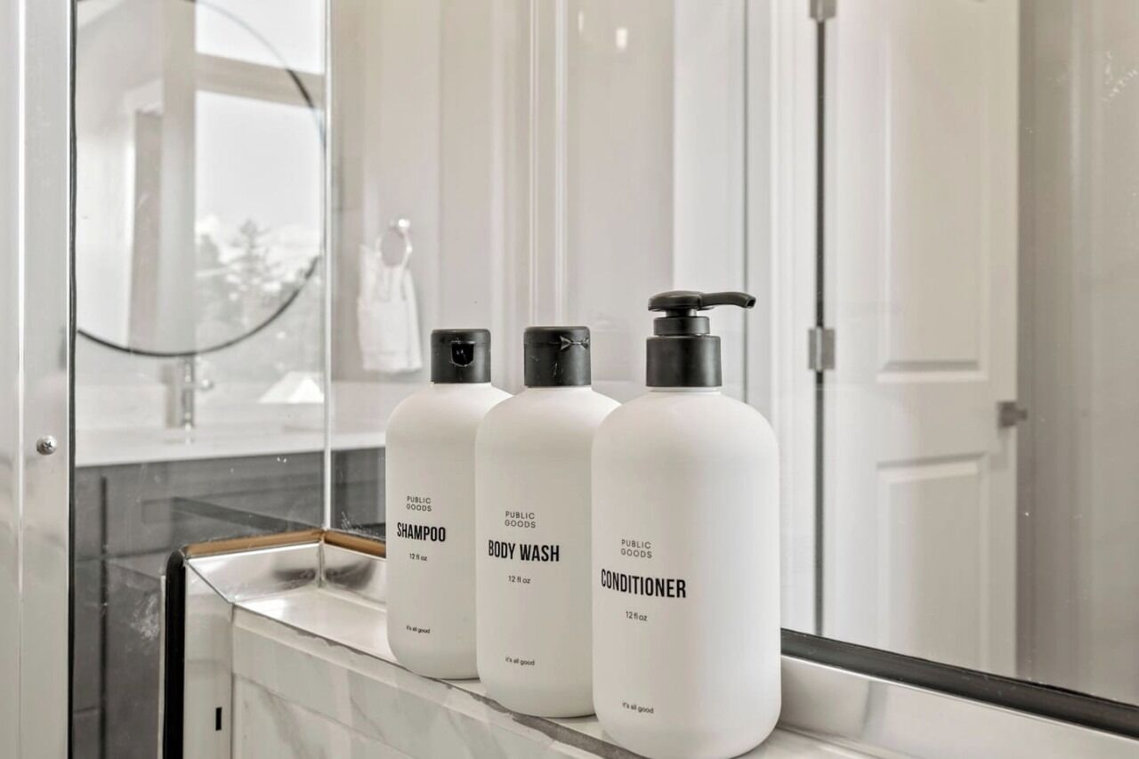 Tres botellas de champú, gel de ducha y acondicionador de Public Goods sobre una encimera de baño.