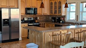 A kitchen with wooden cabinets, stainless steel appliances, a large island with bar stools, and pendant lighting.