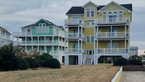 A row of multi-story beach houses with balconies, a grassy area in front, and a cloudy sky.