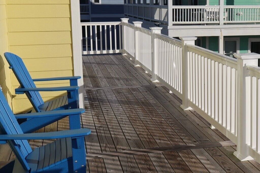 Eine Holzterrasse mit weißen Geländern und blauen Adirondack-Stühlen.