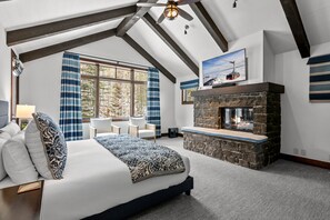 A spacious bedroom with a large bed, a stone fireplace, a ceiling fan, and a window with curtains. - RMR: Granite Ridge Lodge 3209 in Teton Village (Teton Village)