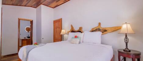 Un dormitorio con una cama grande, cabecera de madera, dos mesitas de noche con lámparas, un espejo y una puerta.