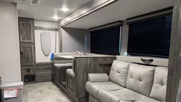 Un intérieur de camping-car compact comprenant un coin cuisine, un espace salon avec des sièges rembourrés et un petit placard de rangement.