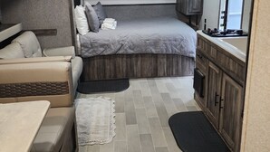 Un intérieur de camping-car compact comprenant un lit, un coin cuisine et un espace salon.