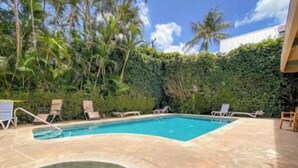 Una piscina con idromassaggio, circondata da lettini e un solarium in pietra.