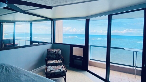 Una camera da letto con un letto grande, una sedia, un tavolino e un balcone con vista sul mare.