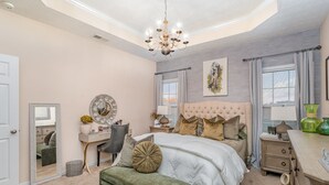 A bedroom with a large bed, a vanity, a desk, and a chandelier.