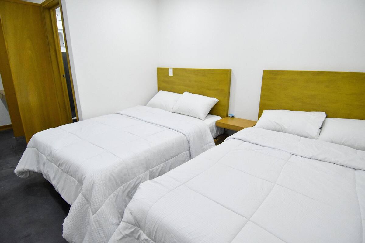 Dos camas individuales con cabeceros de madera en una habitación con alfombra gris.