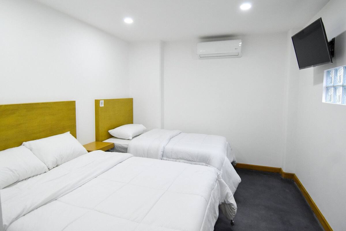 Habitación de hotel con dos camas, un televisor de pantalla plana montado en la pared y un equipo de aire acondicionado.