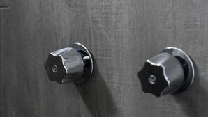 Dues noves manises metàl·liques sobre una porta gris amb superfície rugosa.