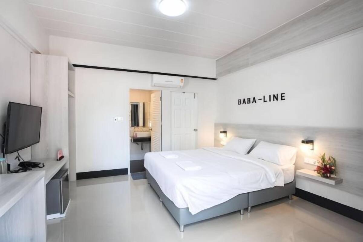 A modern hotel room with a bed, a TV, a desk, and a bathroom visible through an open door.