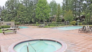 Un área de piscina con jacuzzi, sillas de descanso y mesas de picnic.