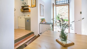 A kitchen with a dishwasher, a wooden shelf, and a window with a view of a stone wall.
