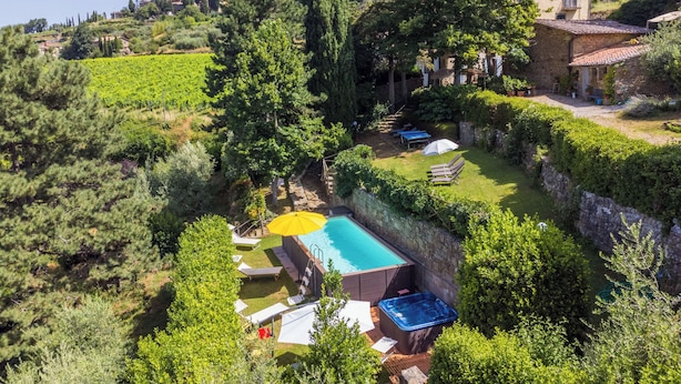 A pool area with lounge chairs and a hot tub, surrounded by lush greenery and a vineyard in the background.