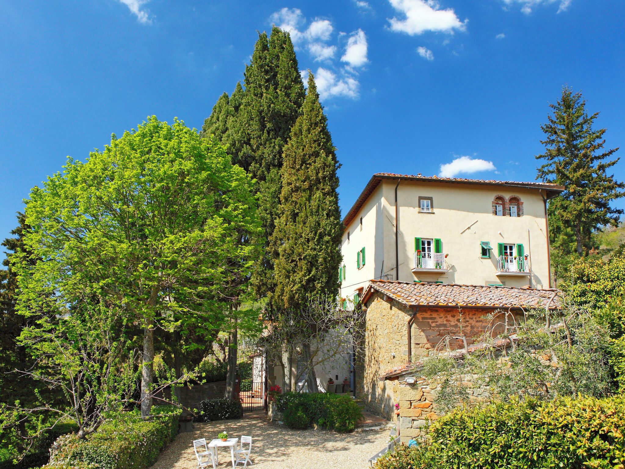 A two-story building with a garden patio, surrounded by trees and a clear blue sky.