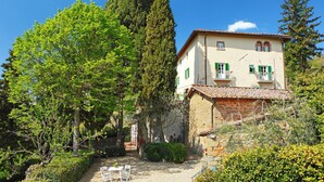 A two-story building with a garden patio, surrounded by trees and a clear blue sky.