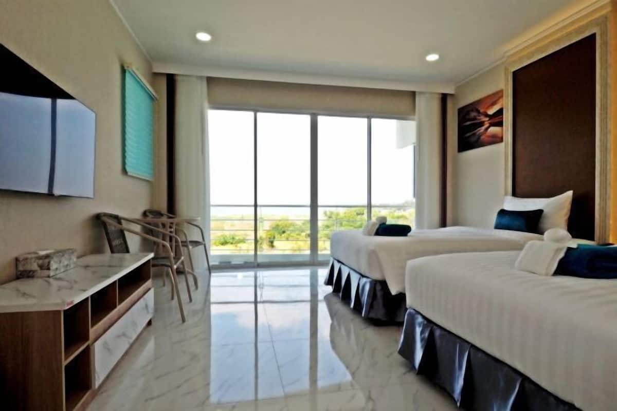 A hotel room with two beds, a desk, and a large window offering a view.