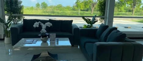 A modern living area with a sofa, a coffee table, and a view of a green landscape.