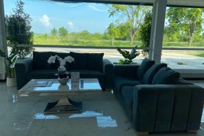 A modern living area with a sofa, a coffee table, and a view of a green landscape. - Siam Sky Pattaya Hotel (Bang Lamung)