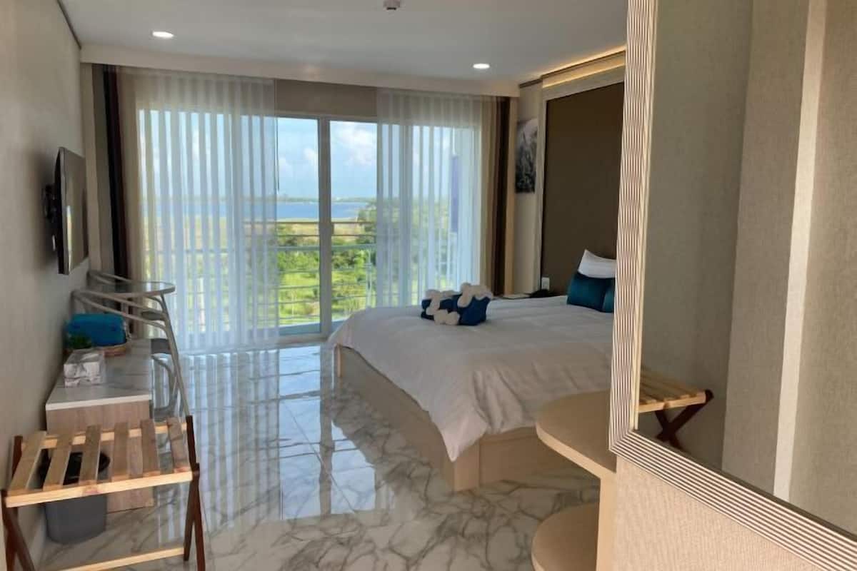 A hotel room with a large bed, a desk, a chair, and a balcony with a view.