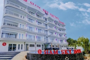 Un hotel de varios pisos con balcones, un cartel que dice 'SIAM SKY HOUSE' y una pared de piedra con el nombre del hotel.