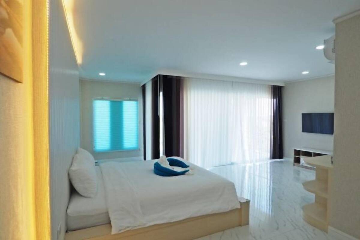 A modern hotel room with a bed, a TV, a desk, and a large window.