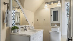Een badkamer met een wit wastafelmeubel, een grote spiegel, een wastafel, een toilet en een raam met gordijnen.