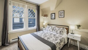 Een slaapkamer met een groot bed, twee nachtkastjes, een raam met gordijnen en een wandplank met een lamp.