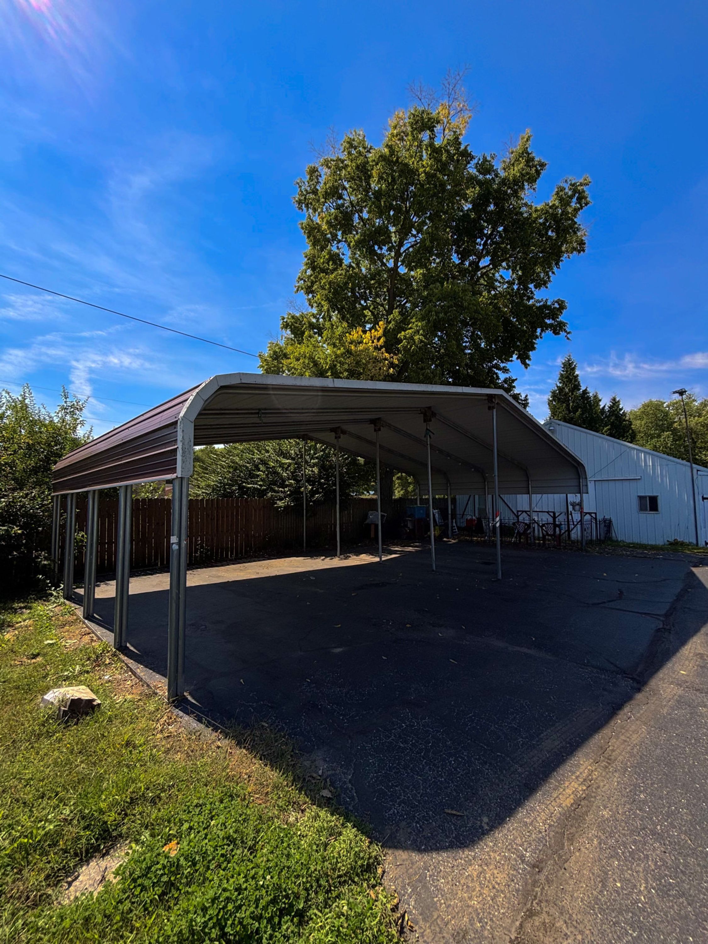 A covered outdoor area with a metal roof, surrounded by a fence, and a building in the background.
