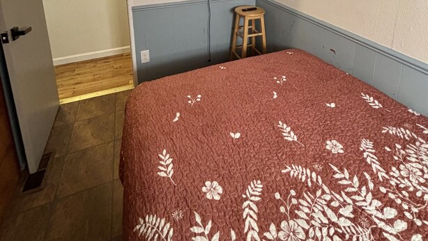 A bedroom with a bed, a television mounted on the wall, a wooden stool, and a door leading to another room. - 4 bd 10 min to Downtown W D (Indianapolis)