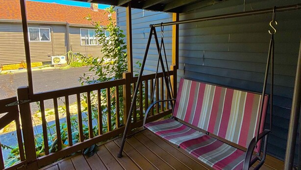 Un porche cubierto con un asiento tipo hamaca y vistas a un barrio residencial.