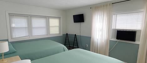 A hotel room with two beds, a TV, and a window with curtains.
