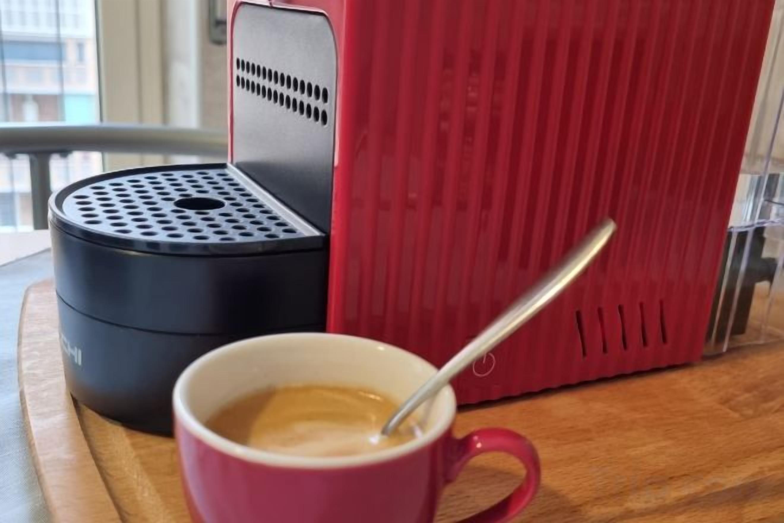 A red mug with a spoon, a black and red appliance, and a window in the background.