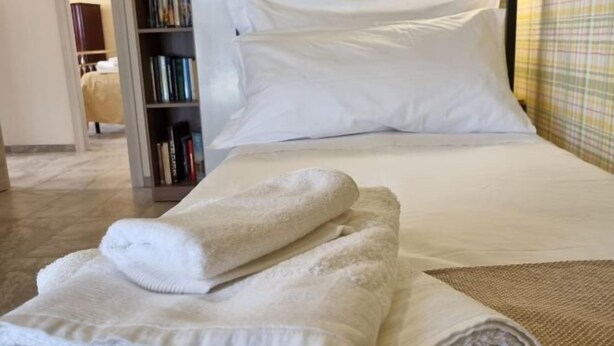 A neatly made bed with white linens and a rolled-up towel on the side. - Happy Home Piramide Cestia Lussuoso Unico Esclusivo a Roma (Rome)