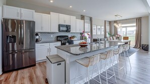 Een moderne keuken met witte kasten, roestvrijstalen apparatuur, een centraal eiland met barkrukken en uitzicht op de omgeving.