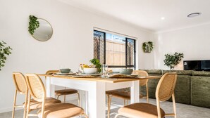 A dining area with a white table, four chairs, and a large window with a view of a fence. - Canopy House - Brand New Home in Nature’s Arms (Greenbank)