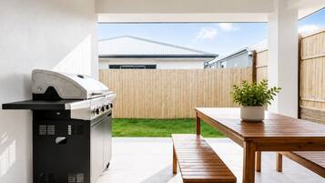 A patio with a grill, a wooden table, and a potted plant.