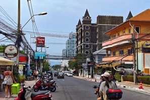 A street with parked motorcycles, a Tops Daily sign, and a building with a pointed roof. - New Nordic Trend 4 by Apartwell (Pattaya)