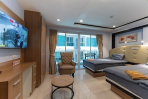 Habitación de hotel con televisión, una silla, dos camas y balcón con cortinas.