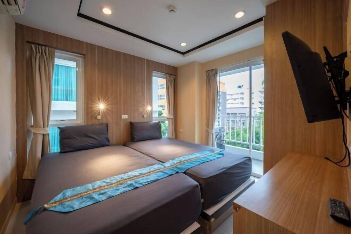 Habitación de hotel con cama, escritorio, televisor y balcón con vistas.