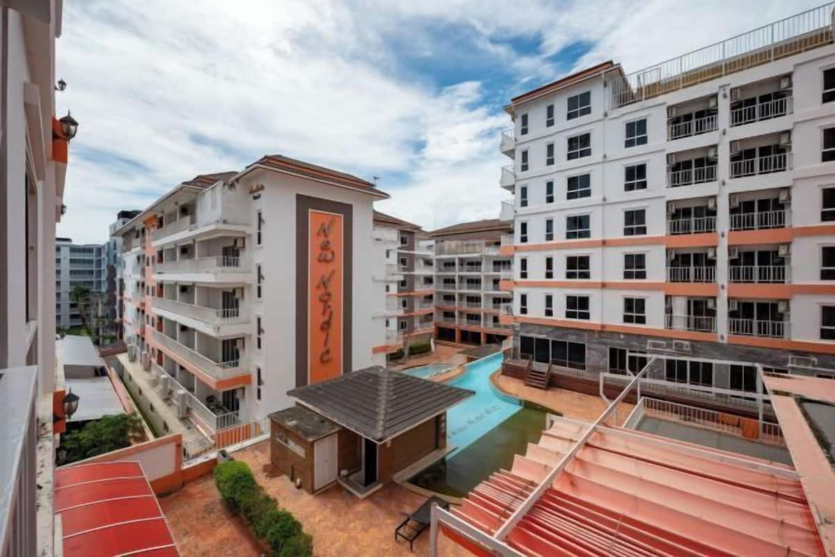 Un edificio residencial de varios pisos con balcones, una piscina y una zona cubierta pequeña.
