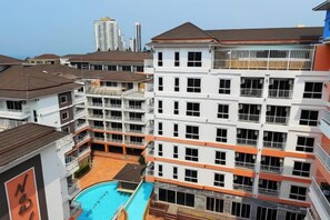 A multi-story hotel with balconies, a swimming pool, and a view of the cityscape. - New Nordic Trend 4 by Apartwell (Pattaya)