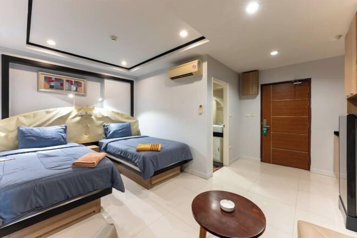 Habitación de hotel con dos camas, una mesita, un armario y un equipo de aire acondicionado.