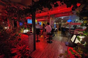 Een bar met houten vloer, barstoelen en rode verlichting.