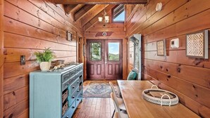 A wooden cabin interior with a dining table, a blue cabinet with baskets, and a view through the door.